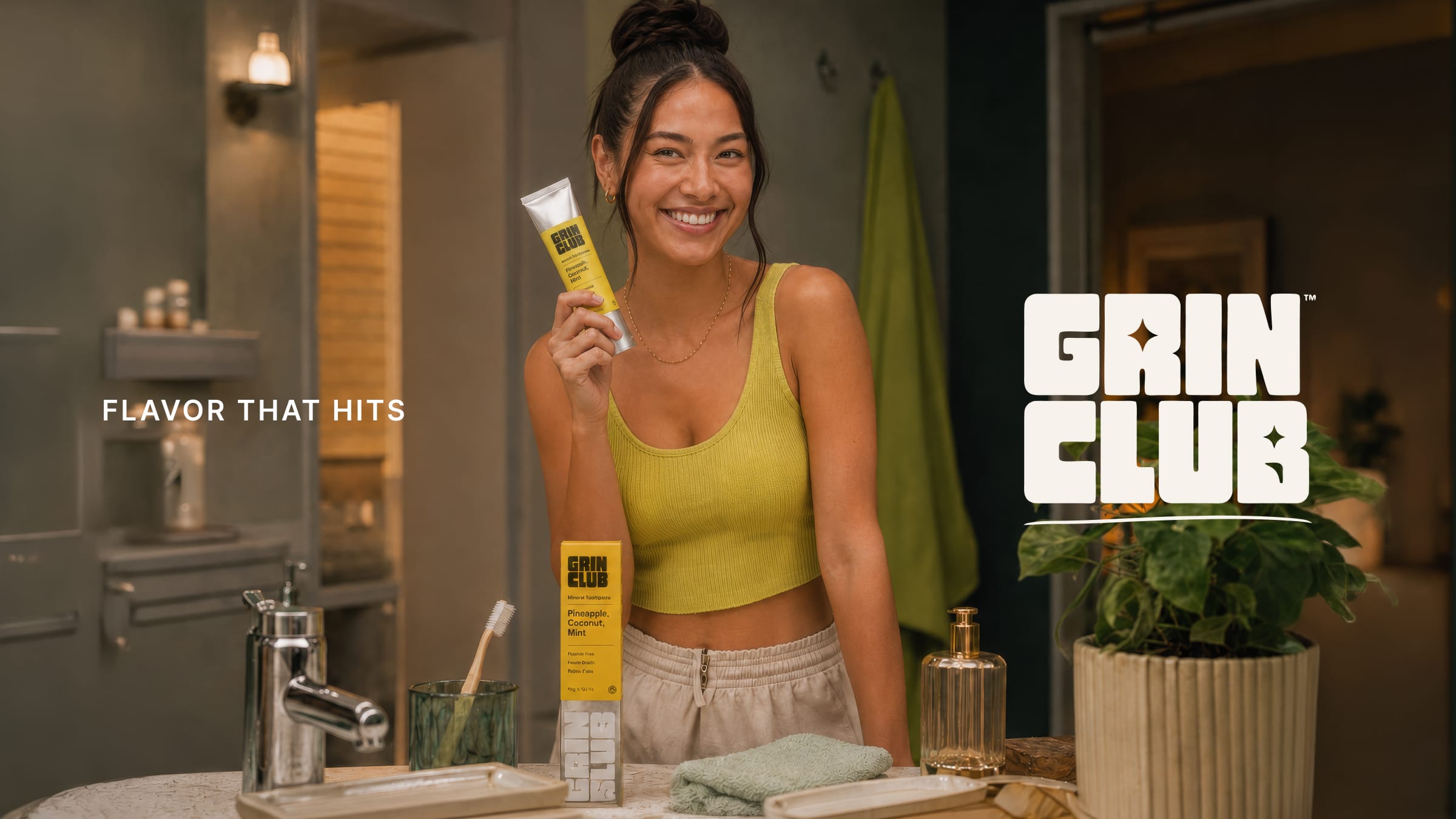 A smiling woman holding a yellow Grin Club tube in her bathroom.