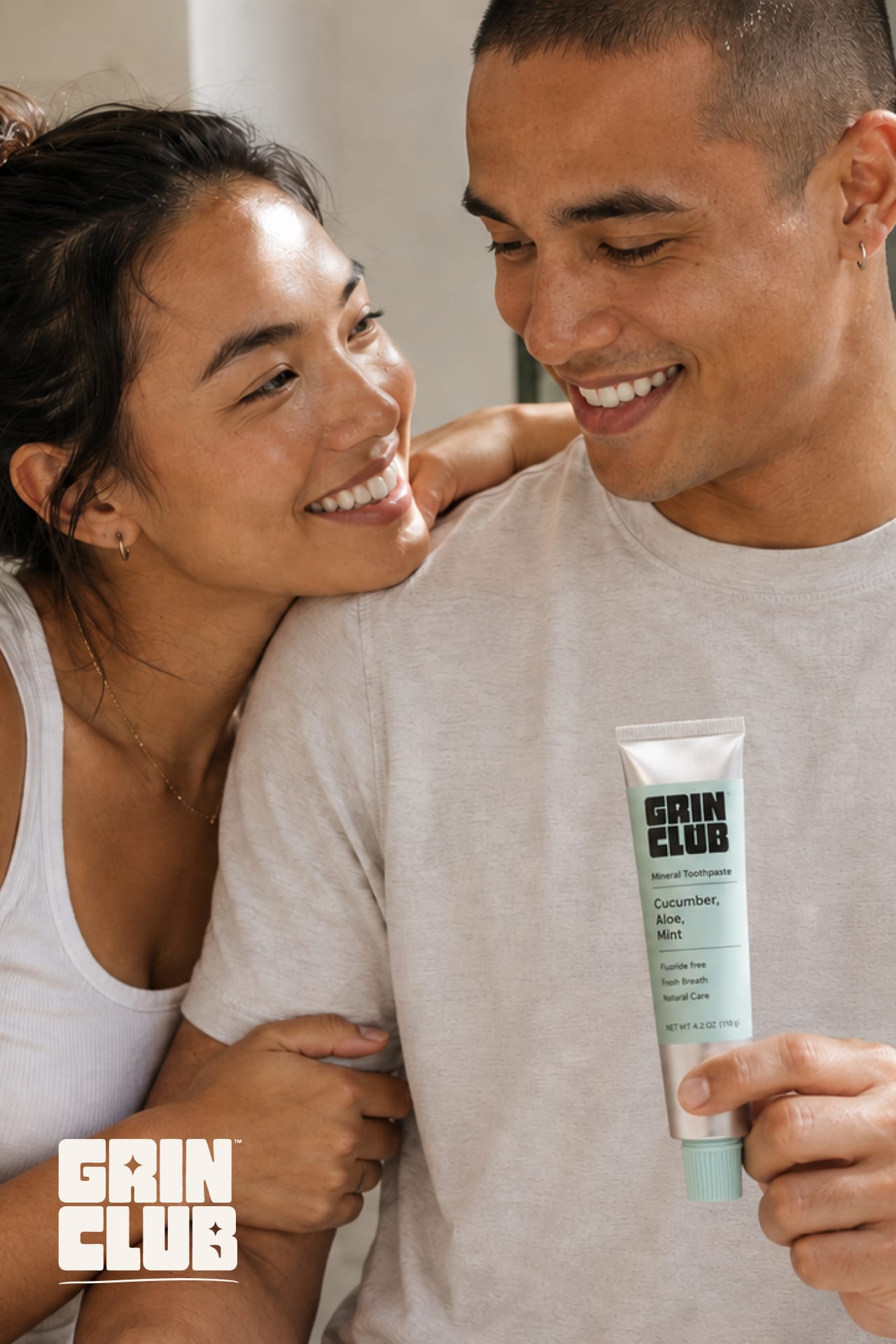 A smiling couple, the man holding a mint-green Grin Club tube.