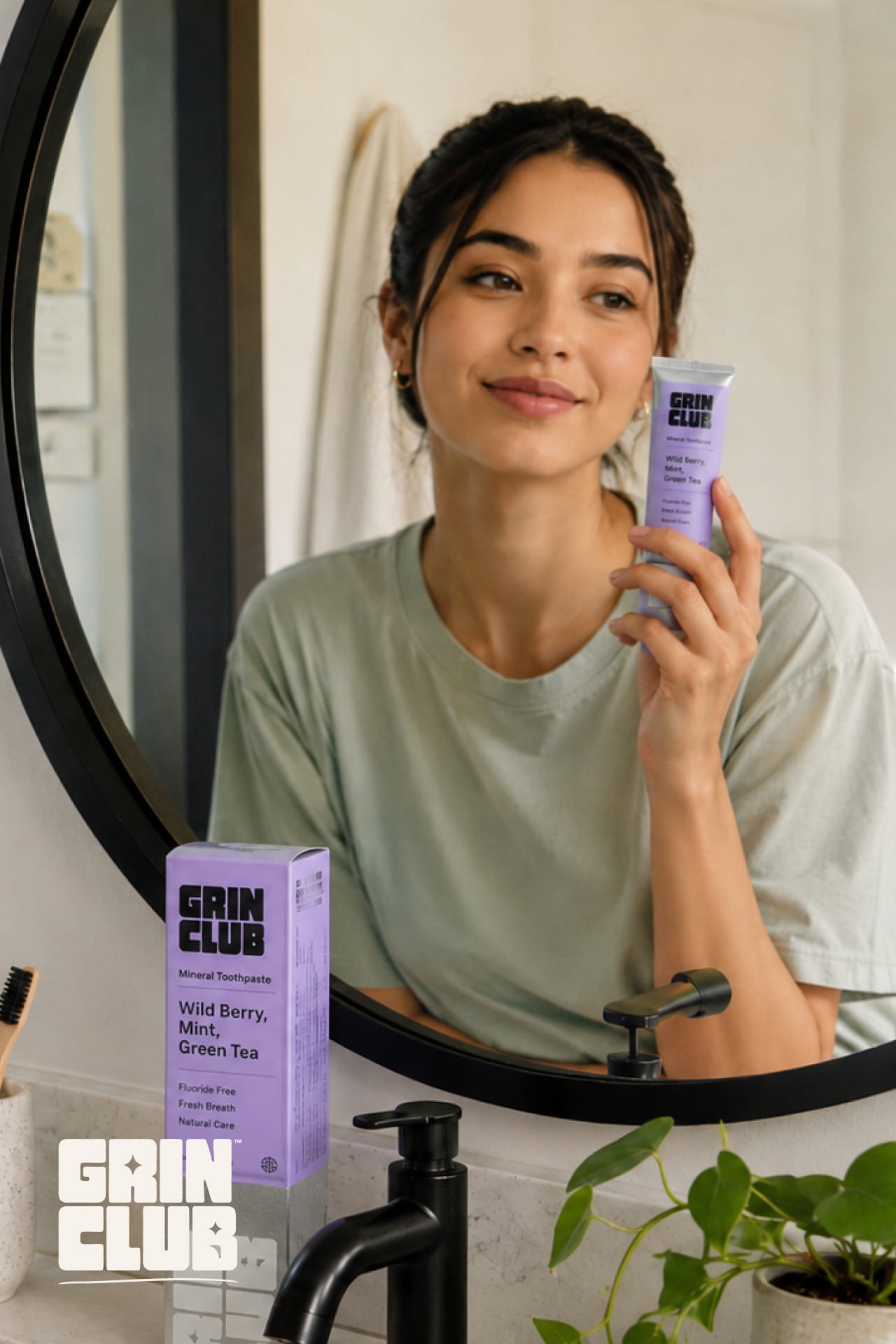 A woman at a bathroom mirror holding a lilac Grin Club tube.
