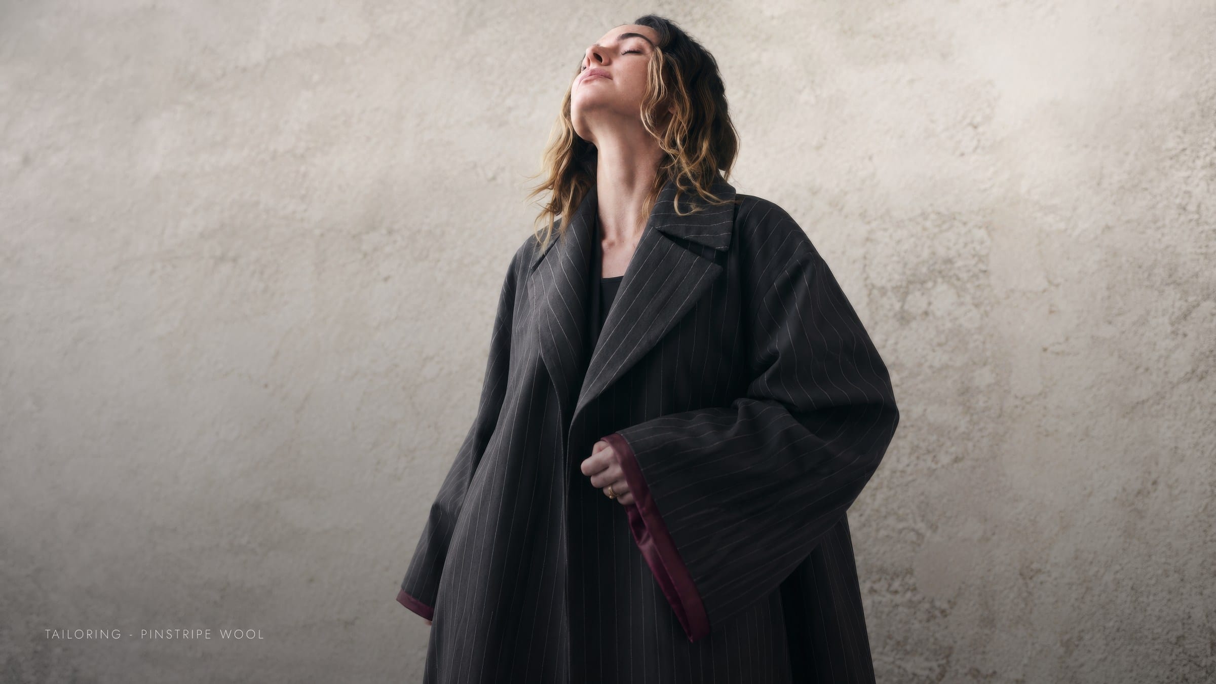 A pinstripe wool abaya photographed against a plaster wall.