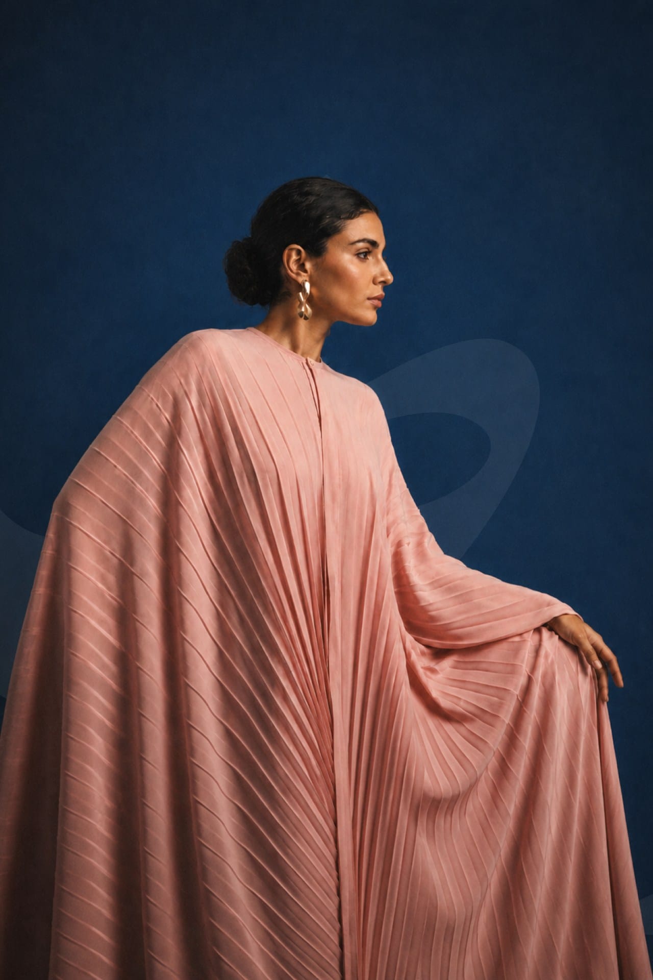 A dusk-pink pleated abaya in profile against deep cobalt.