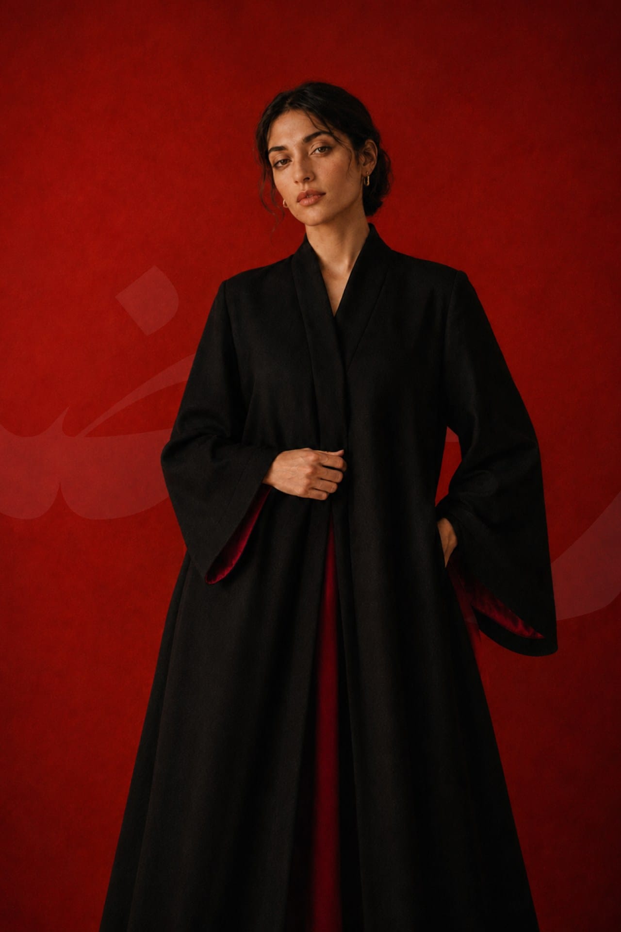 A black abaya lined in oxblood against a red wall.