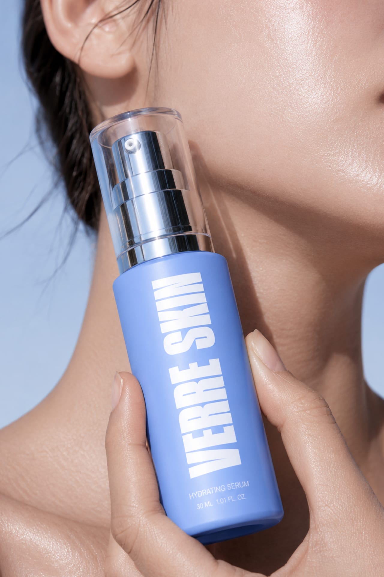 A woman holding the Verre Skin serum against her jaw.