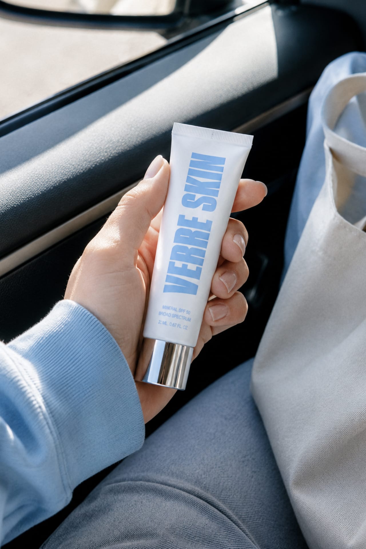 A hand holding the Verre Skin mineral SPF tube in a car.